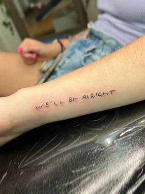 A woman with her arm that has the words " we 'll be alright ".