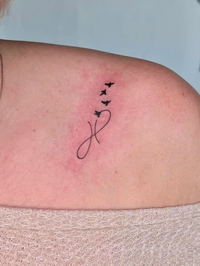 A tattoo of the letter j with birds flying around it.